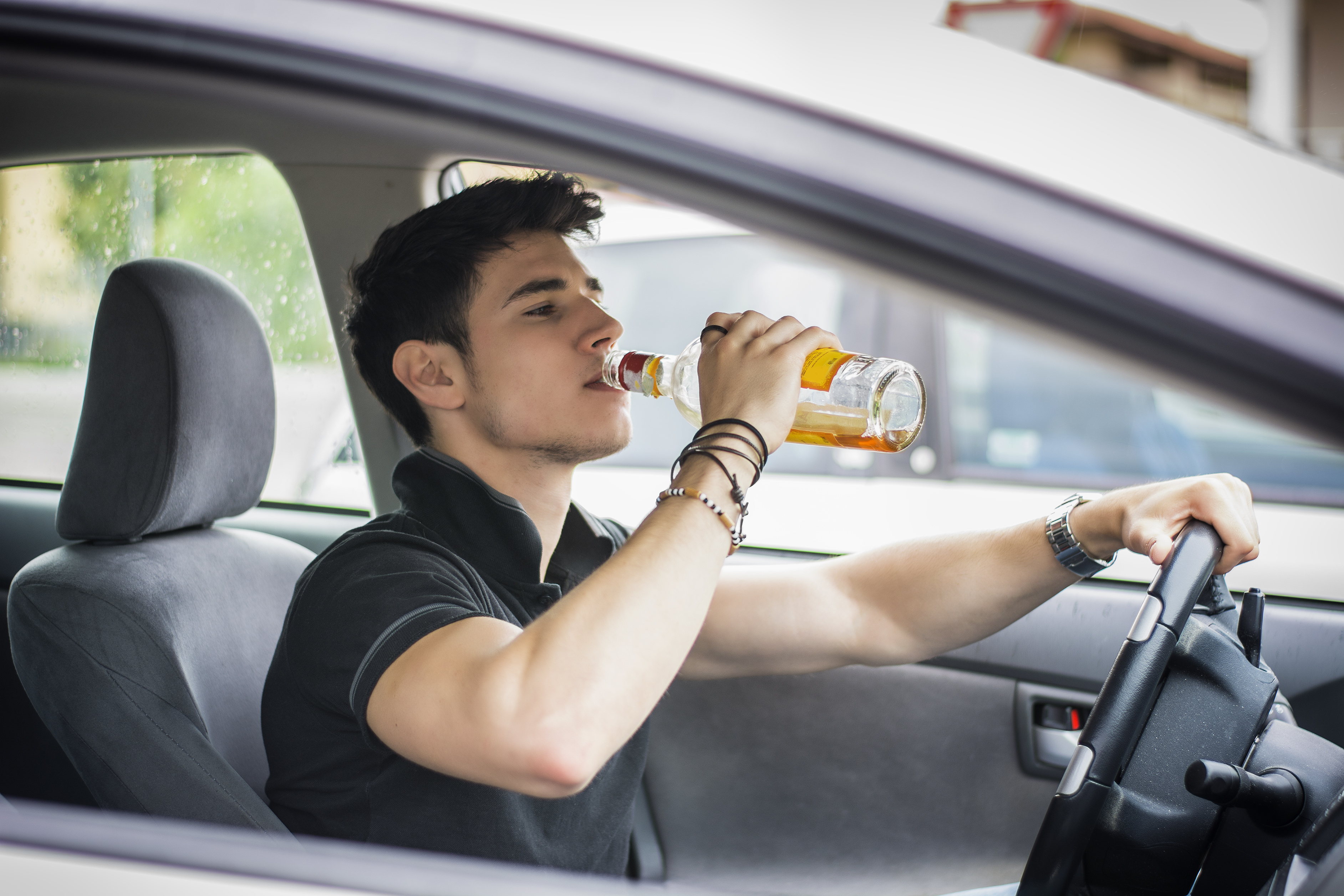 Young handsome man driving his car while drinking alcohol in the traffic